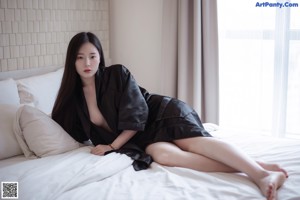 A naked asian woman laying on a bed in a black robe.
