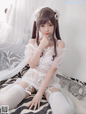 A woman in a white dress and stockings sitting on a white rug.