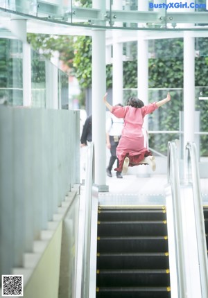 A woman in a pink coat is standing on an escalator.