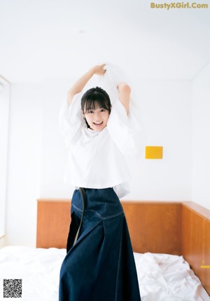 A woman in a white shirt and blue skirt jumping on a bed.