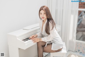 A woman in a white shirt and black stockings sitting on a bed.