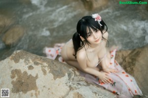 A woman in a bikini standing on a rock by the water.