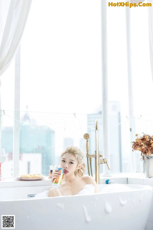 A woman sitting in a bathtub drinking from a bottle.
