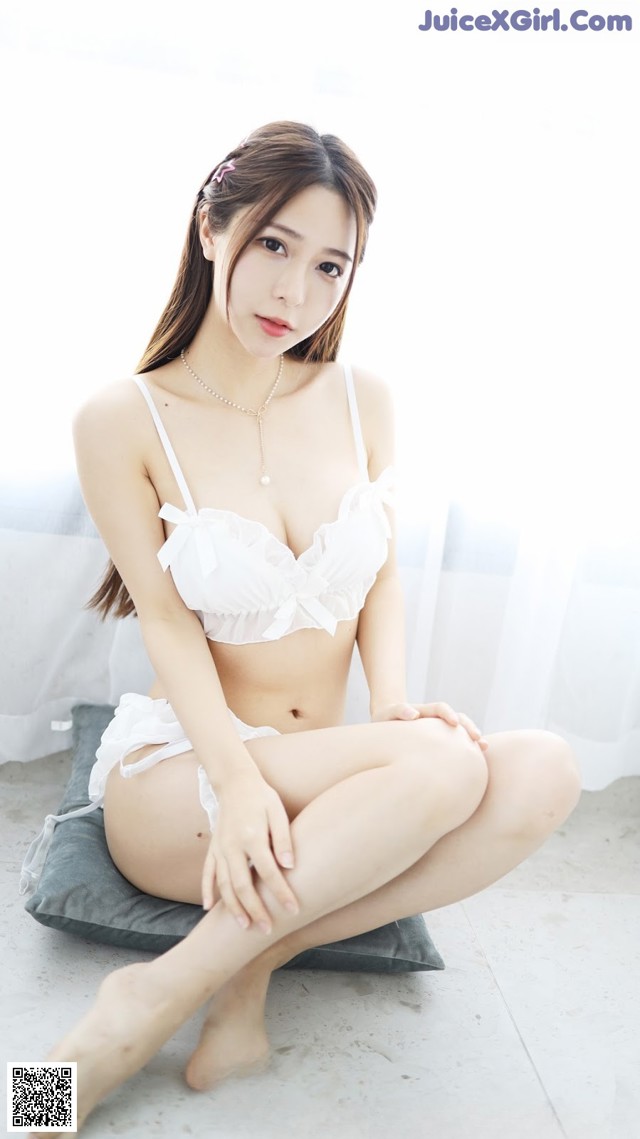 A woman in a white lingerie sitting on a pillow.