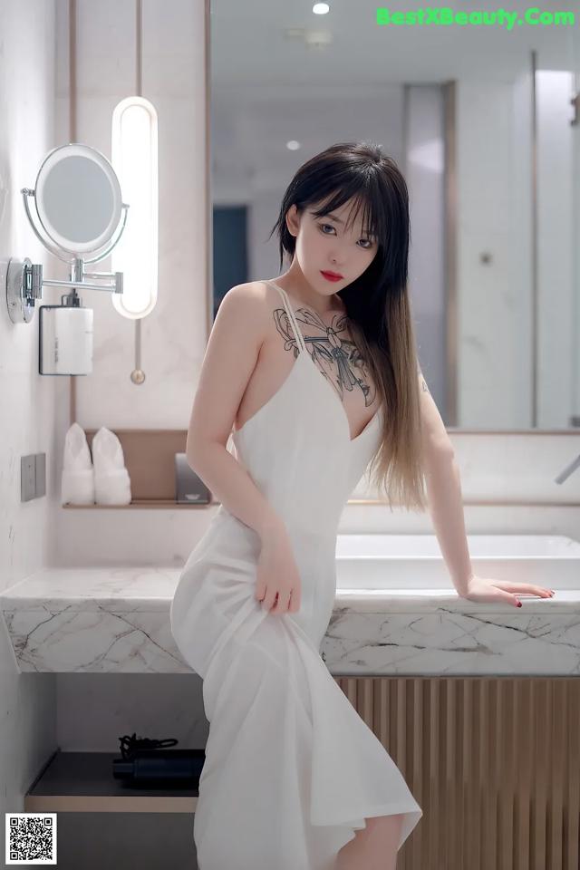 A woman in a white dress standing in front of a mirror.