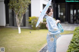 A woman in a blue and pink kimono sitting on a chair.