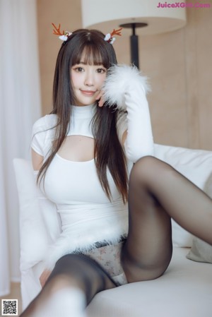 A woman in a white dress posing on a white couch.