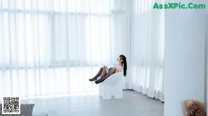 A woman sitting on top of a white chair in front of a window.