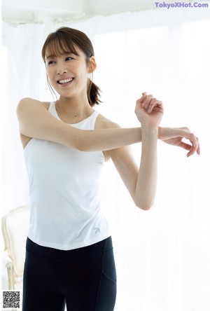 A woman standing in front of a white wall wearing a blue sweater.