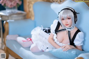 A woman in a maid outfit sitting on a blue couch.