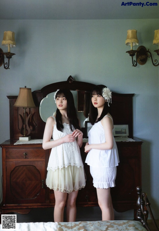 Two young women standing next to each other in a bedroom.