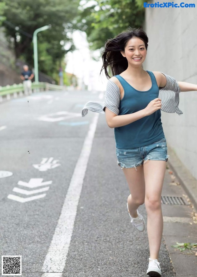 A woman in shorts and a tank top is running down the street.