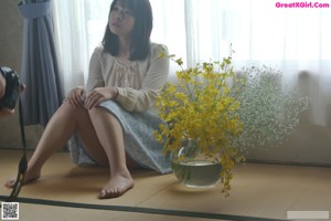 A naked woman standing in front of a window holding a vase of flowers.