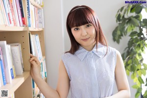 A young woman sitting on the floor in front of a bookshelf.