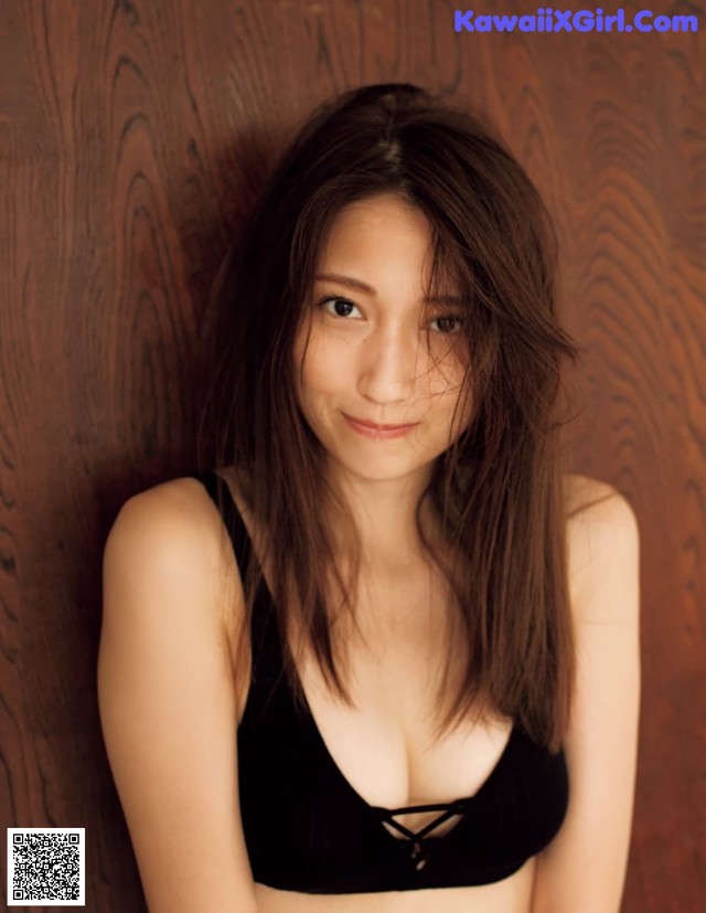 A woman in a black bra top leaning against a wooden wall.