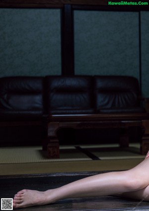 A naked woman sitting on a wooden floor next to a window.