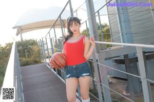 A woman in a red tank top and denim shorts holding a basketball.