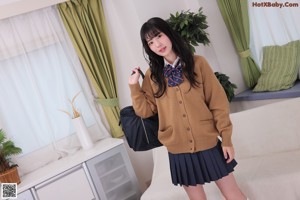 A young woman sitting on a white couch wearing a school uniform.