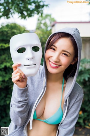 A woman in a blue bikini holding a white mask.